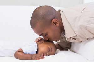 Adorable baby boy sleeping while being watched by father at home